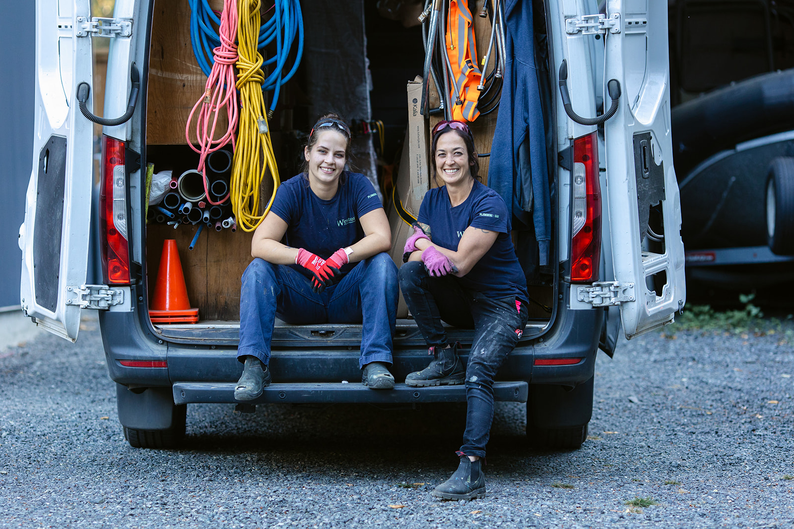 Two female tradespeople sitting at the back of a truck with supplies.