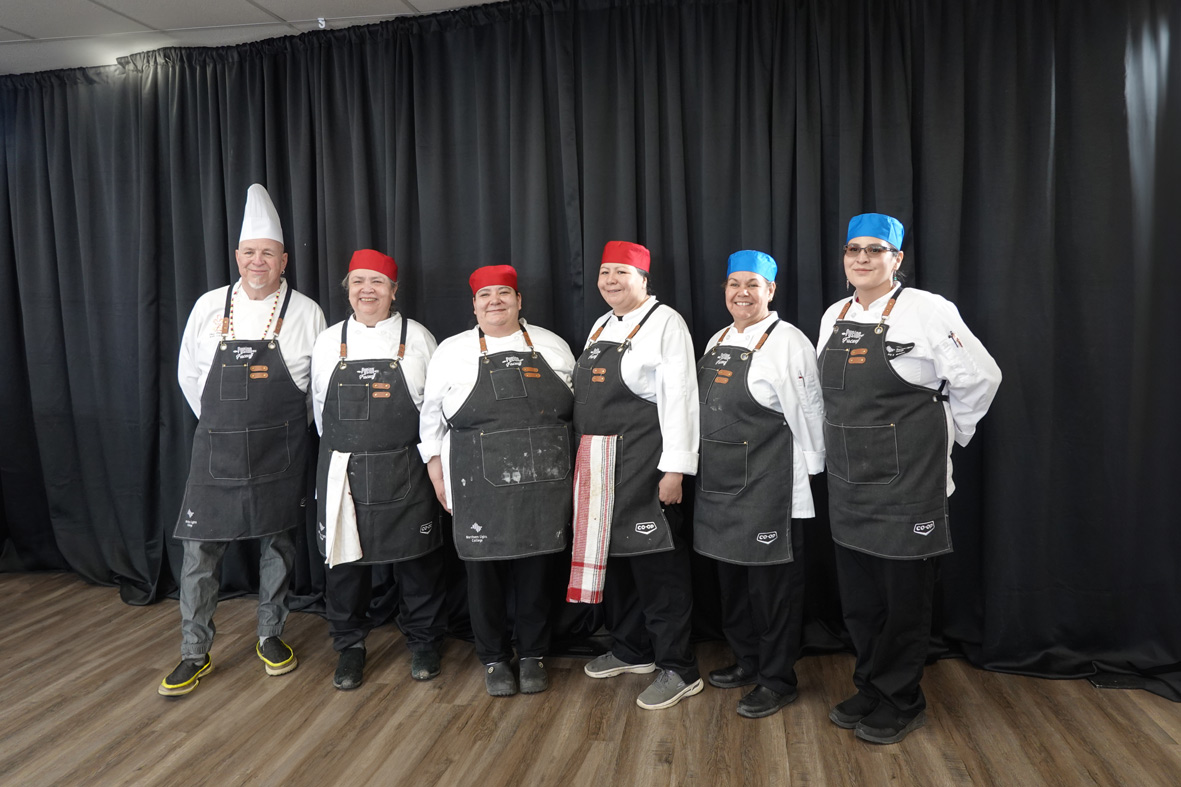 Culinary students and instructor standing against black cloth backdrop