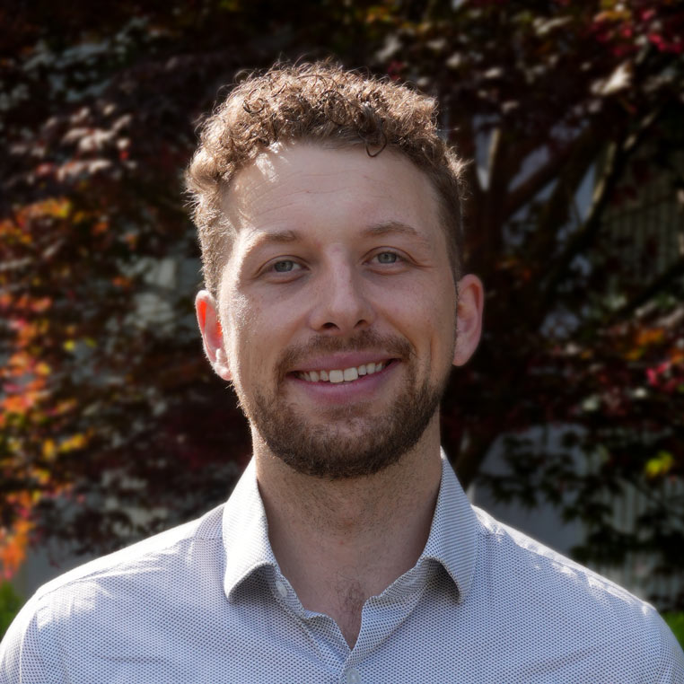 man with curly brown hair and trees in background