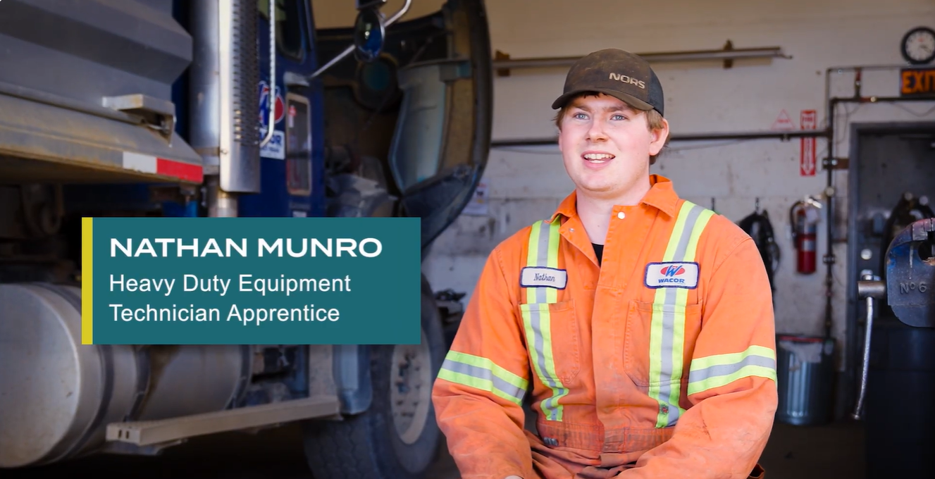 Nathan sitting in shop wearing orange overalls in front of a heavy duty truck