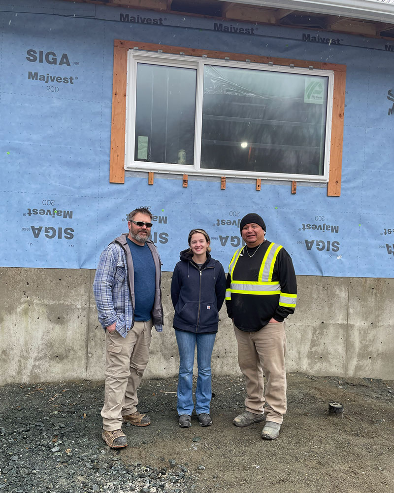 three people standing in front of concrete wall of a building on gravel floor