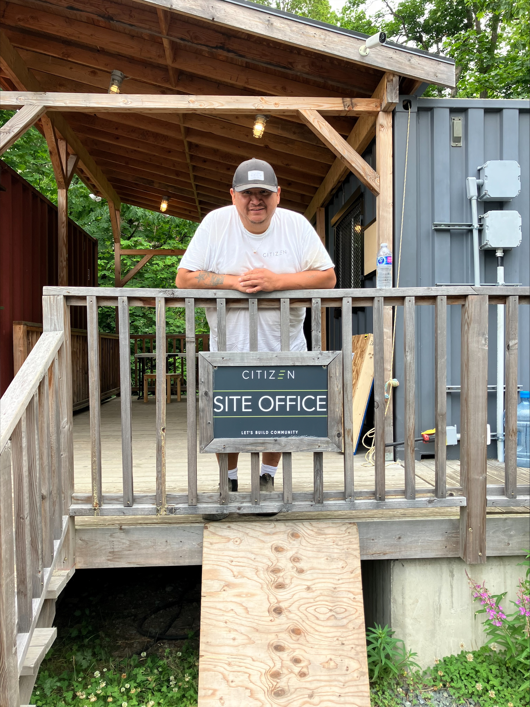 man with black hat standing on wooden porch in front of sign