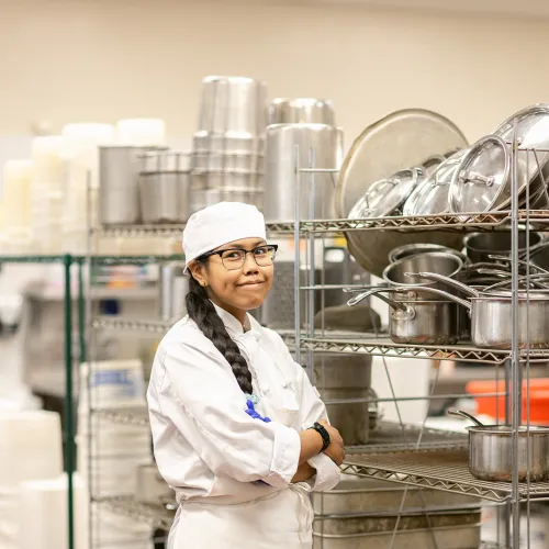 A woman in cooking attire standing in a kitchen. 