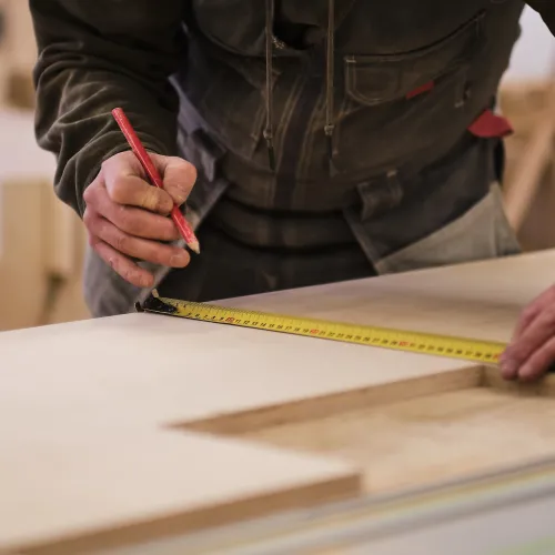 person measuring wood with measuring tape and pencil