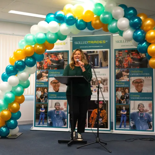 Shelley standing at microphone with balloons in background