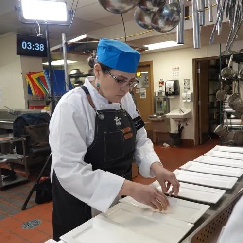 chef with blue cap plating in kitchen