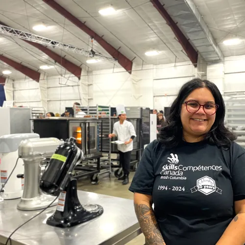 Former gold medalist smiling and standing in front of baking area of the Skills Canada BC competition