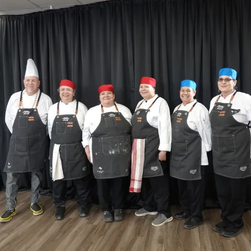 Culinary students and instructor standing against black cloth backdrop