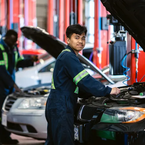 Automotive Service Technicians in garage working on hood of cars