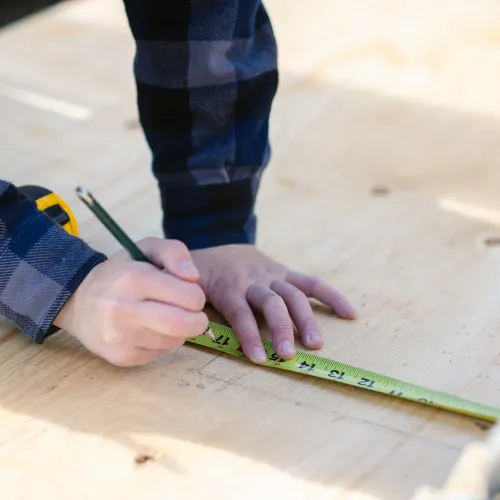 hands holding a pencil and making a line with a measuring tape on plywood