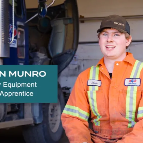 Nathan sitting in shop wearing orange overalls in front of a heavy duty truck